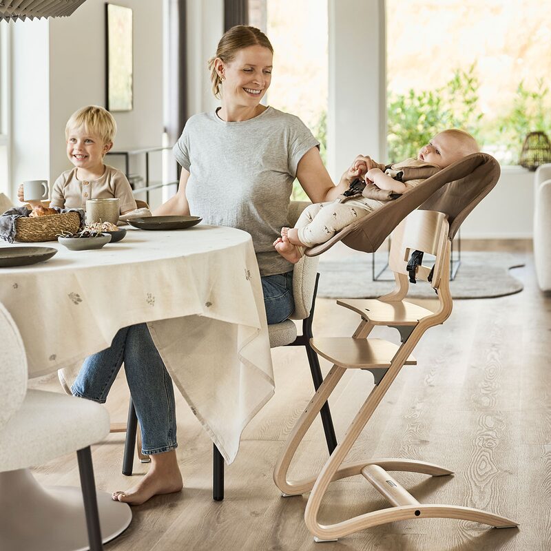 Leander Newborn Seat Mocca — rodzina przy stole, miminko w foteliku na krzesełku Leander