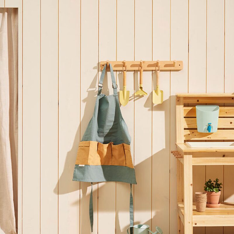 Kids Concept zahradnická zástěra Kids Hub zavěšená na dřevěném věšáku